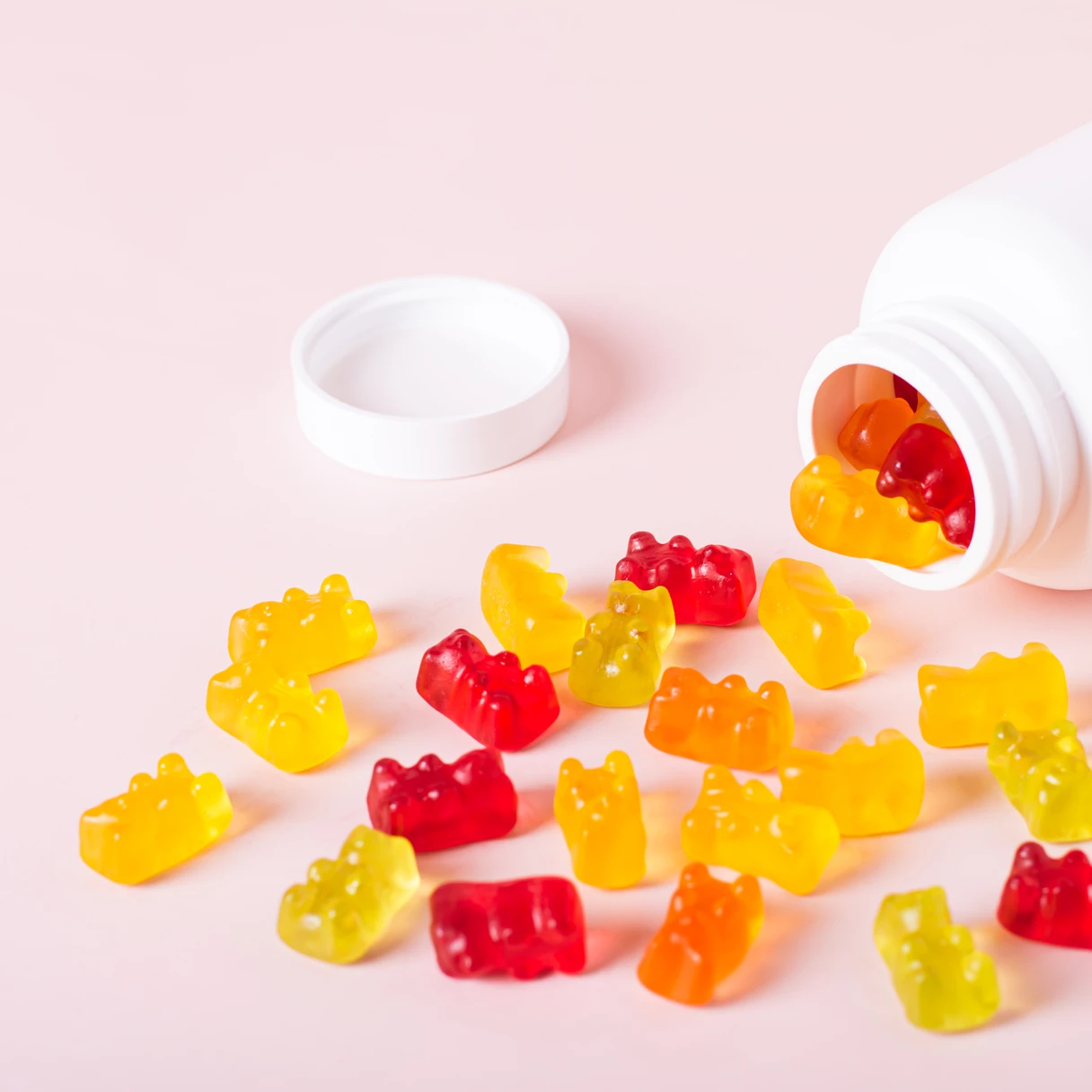 Gominolas con forma de oso saliendo de un bote blanco de suplemento