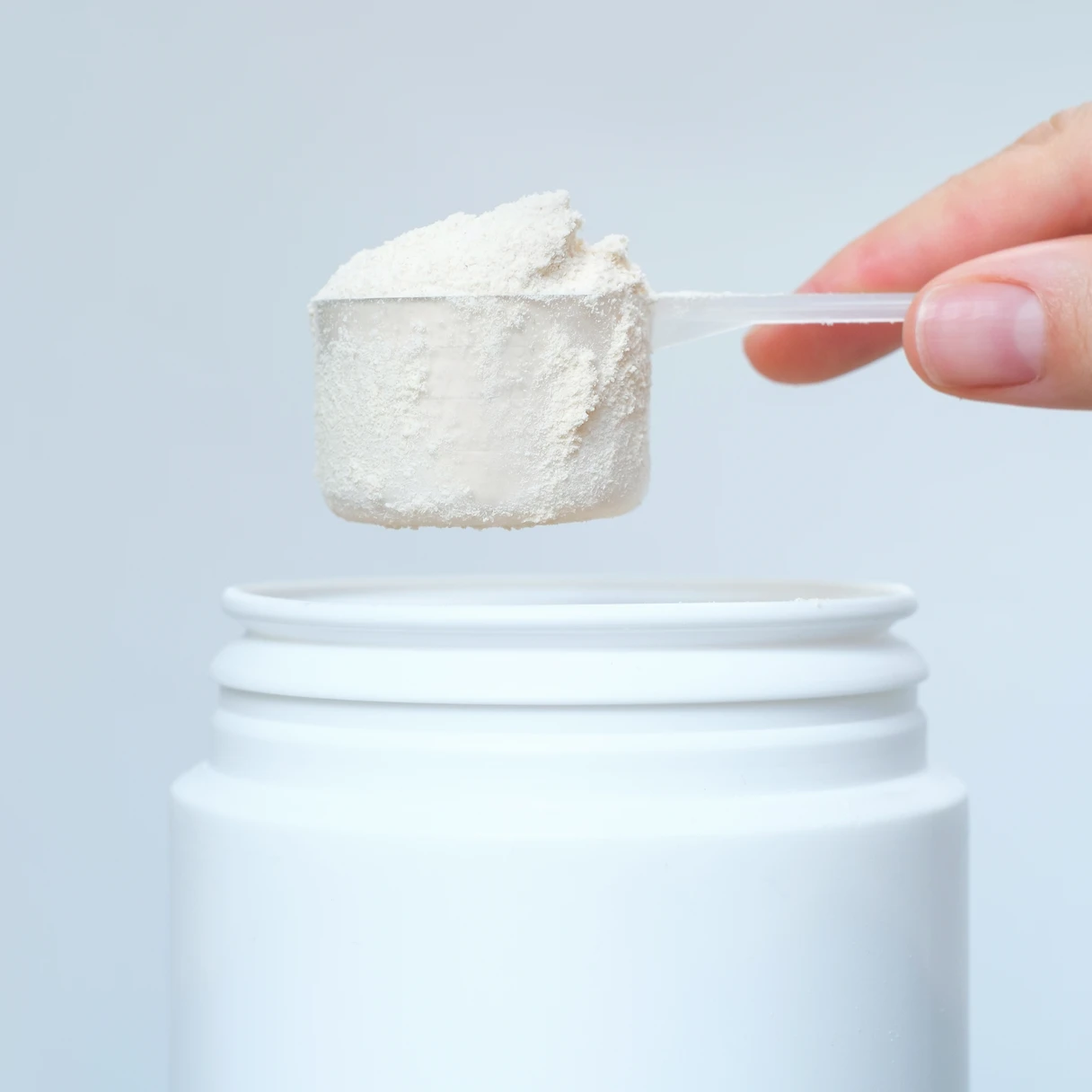 Cacito con proteína en polvo sobre un bote blanco de suplemento