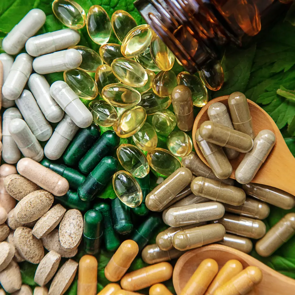 Cápsulas de suplementos vegetales sobre hojas verdes junto a un frasco ámbar